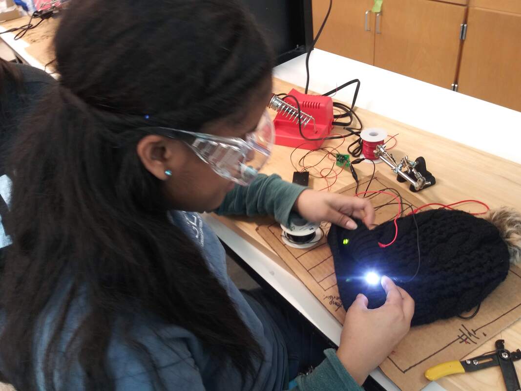 Photo of a student wearing safety goggles and working with a small object with wires and a light