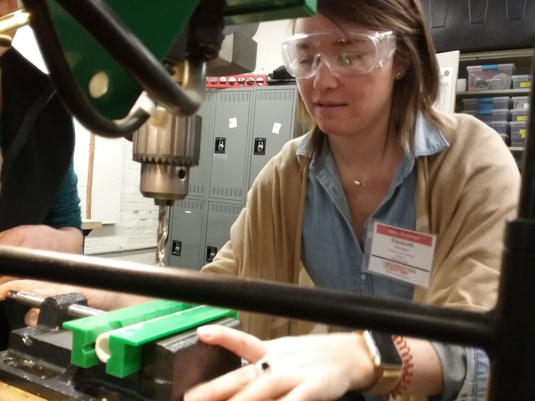 Person wearing safety goggles and a nametag using a drill press