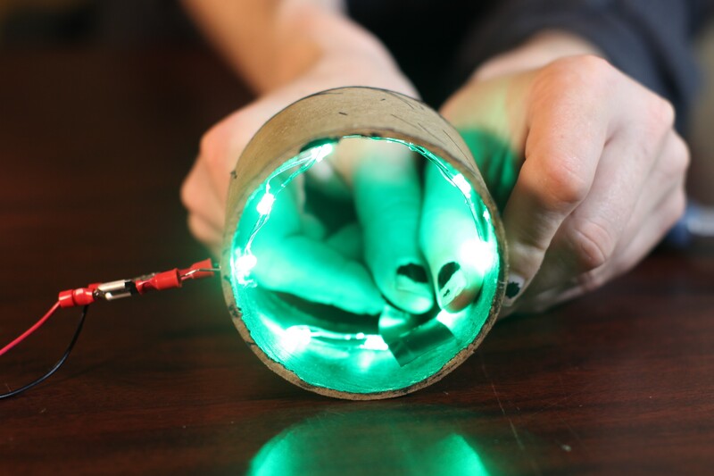 two hands holding a cardboard ring, illuminated from the inside with changeable color LEDs