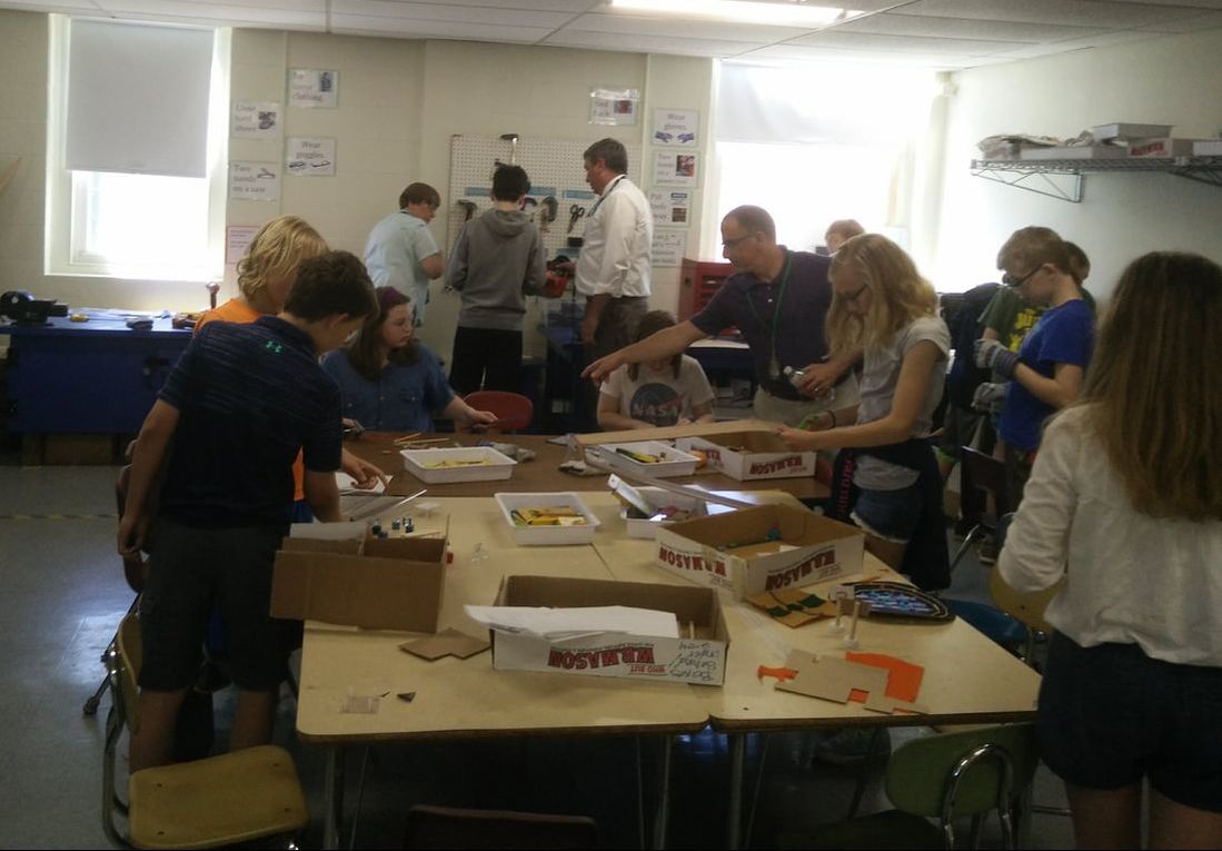 Photo of a busy maker space full of people with large tables covered in projects