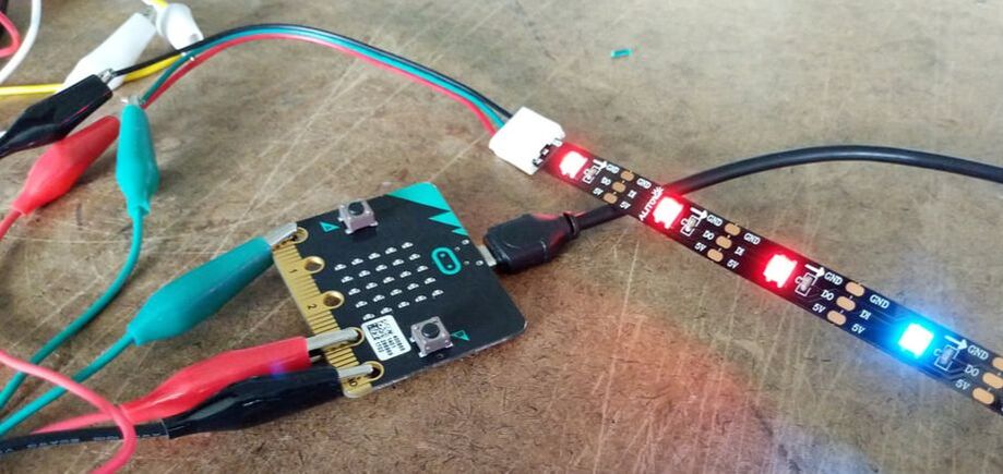 photo of microbit linked to many colorful wires and lighting up a strip of LEDs