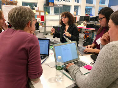 Photo of teachers around a table with laptops out listening Diane lecture