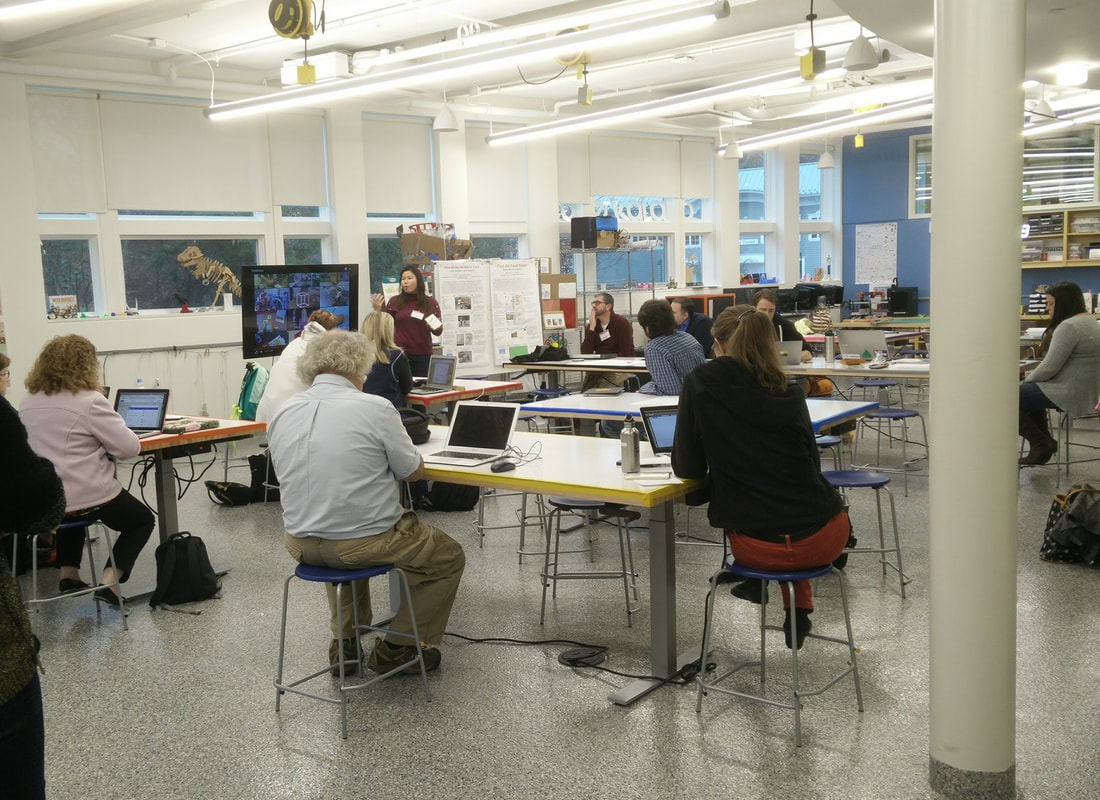 Large, bright classroom where adults are sitting with laptops watching a presentation