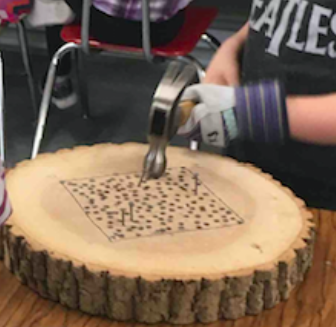 a 1st grader hammers nails into a decorative wooden stepping stone